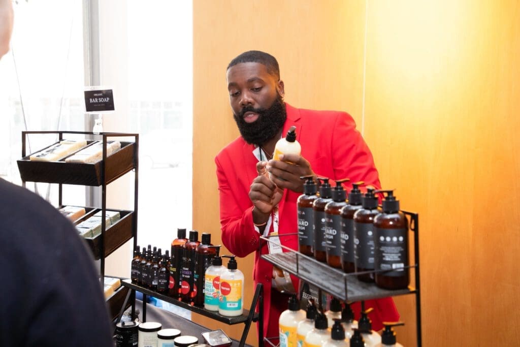 Scott Boateng holds and points to a bottle of body wash from Preva Body as he talks to a customer