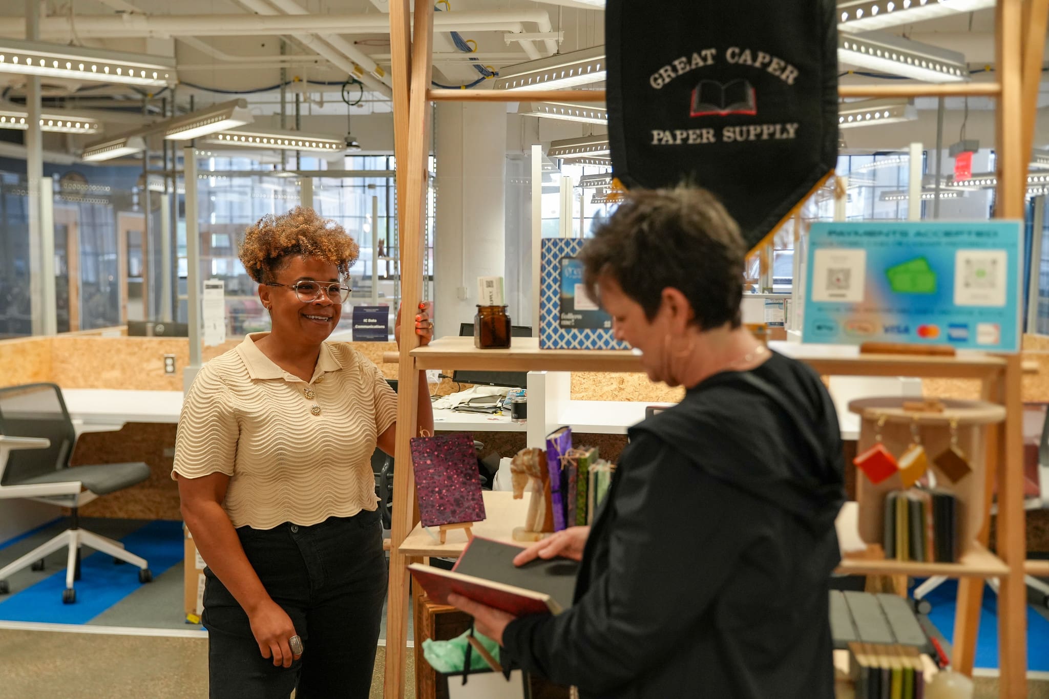 A shop owner with a pop-up vendor booth talking to a custimer about the products they are selling.