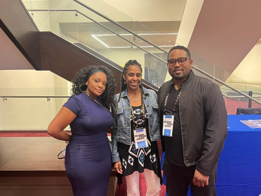 Two women and one man stand next to each other and smile for a photograph.